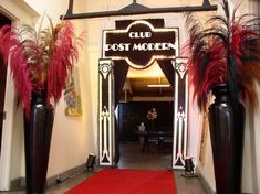 an entrance to a restaurant with red carpet and tall black vases on either side