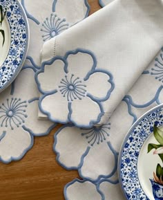 blue and white plates with flowers on them sitting on a wooden table next to napkins