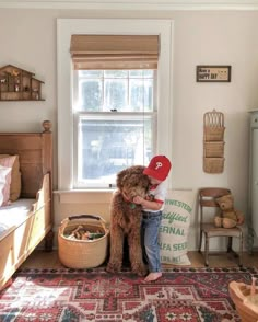 a young boy hugging his dog in the corner of a room with a red hat on