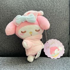 a pink stuffed animal sitting on top of a couch next to a tag with a name