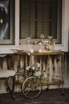 a gold bar cart with candles and flowers on the table in front of a window