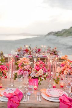 the table is set with pink and white plates, silverware, and flower centerpieces