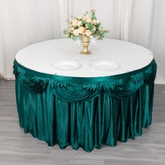 a round table with two white plates on it and green drapes around the top