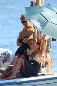 a man and two women sitting on the back of a sailboat under an umbrella