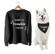 a white dog sitting next to a black shirt that says, where i go trouble follows