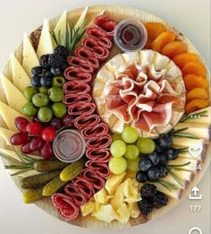 a platter filled with different types of cheeses, meats and fruit on top of each other