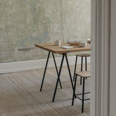 a wooden table with two chairs next to it on a hard wood floor in front of a wall