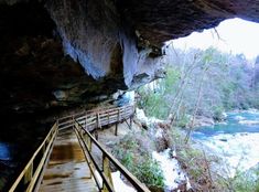 a wooden walkway leading to a cave with water running through it and snow on the ground