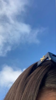 a woman's hair with scissors on top of it and clouds in the background