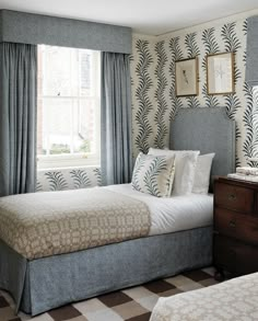 two beds in a bedroom with patterned wallpaper and curtains on the window sill