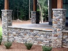 an outdoor patio with stone pillars and plants in the foreground, surrounded by pine trees