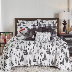 a bed covered in black and white christmas trees on it's comforter, next to a night stand