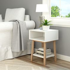 a nightstand with books and a potted plant on it next to a white couch