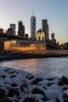 the city skyline is lit up at night with snow on the ground and rocks in front of it