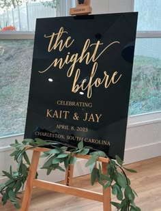 a black and gold wedding sign with greenery on the easel in front of a window