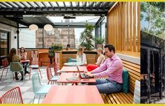 people are sitting at tables with laptops in an open air restaurant, while one person is on the phone