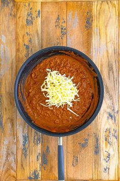 a bowl filled with chili and cheese on top of a wooden table