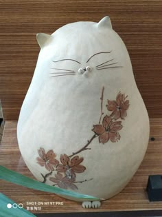 a white cat sitting on top of a wooden table next to a green planter