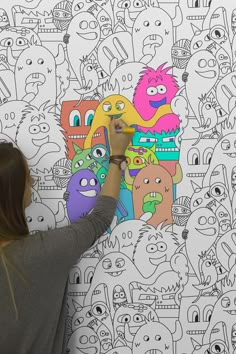 a woman is drawing on a wall with colorful cartoon characters in the background and behind her