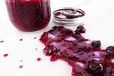 a jar filled with blueberry jam next to a spoon on top of a table