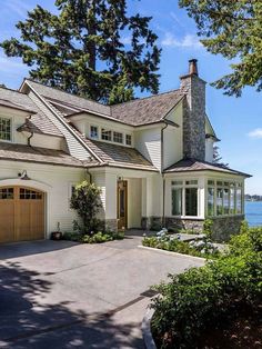 a large white house with lots of windows and trees in front of the water on a sunny day