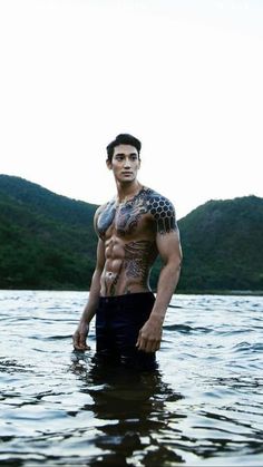 a man standing in the water with tattoos on his chest and arm, looking at the camera