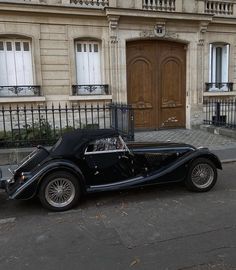 an old black car parked in front of a building