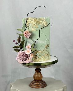 a green and gold wedding cake with pink flowers on the top, sitting on a pedestal