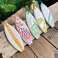 four ceramic surfboards are hanging on a wooden plank next to a christmas tree and pine branches