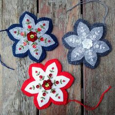 three flower ornaments are hanging on a wooden surface with red, white and blue thread