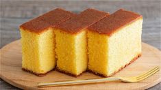 three pieces of yellow cake sitting on top of a wooden plate next to a fork