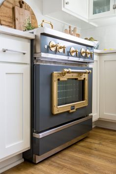 an oven in the middle of a kitchen with white cabinets and wood flooring,