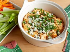 a white bowl filled with food next to celery and carrots on a table