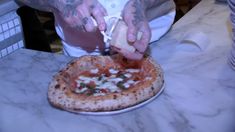 a man cutting into a small pizza on top of a white plate with toppings