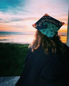 a person wearing a graduation cap with the sun setting in the background and water behind them