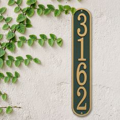 a house number sign on the side of a building with green plants growing around it