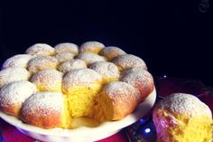 a cake with powdered sugar on top sits next to a plate full of pastries