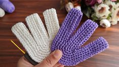 two crocheted gloves are being held up by someone's hand with a knitting needle