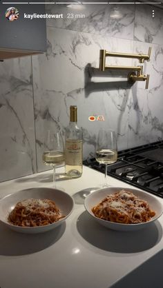 two bowls of food sit on a counter next to a bottle of wine and glasses