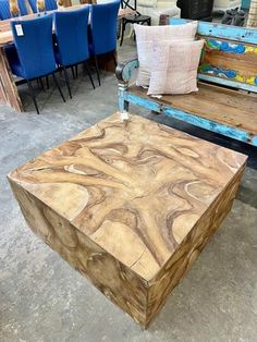 a wooden table sitting on top of a cement floor next to blue chairs and tables