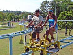 a man and woman riding on a roller coaster at a park with trees in the background