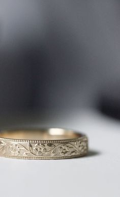 a wedding band with an engraved design on the side, sitting on a white surface