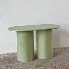 two round green tables sitting next to each other on cement floored area with white wall in background