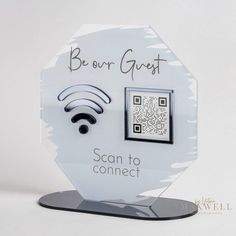 a white and black sign with a wifi symbol on it that says be our guest scan to connect