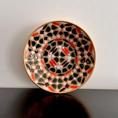 an orange and black plate sitting on top of a table next to a white wall