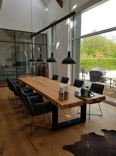 a wooden table surrounded by black chairs in a room with large windows and wood flooring