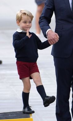 a little boy in red shorts and a suit holds the hand of his father