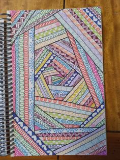 an open spiral notebook with colored paper on top of it and a wooden table in the background