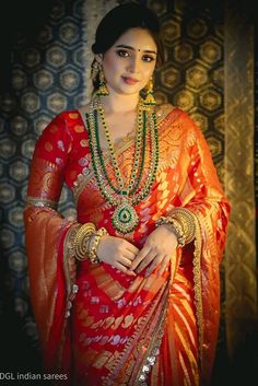 a woman in an orange and red sari with gold jewelry on her neck, standing next