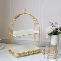 a gold birdcage with flowers in it on a marble countertop next to a white vase